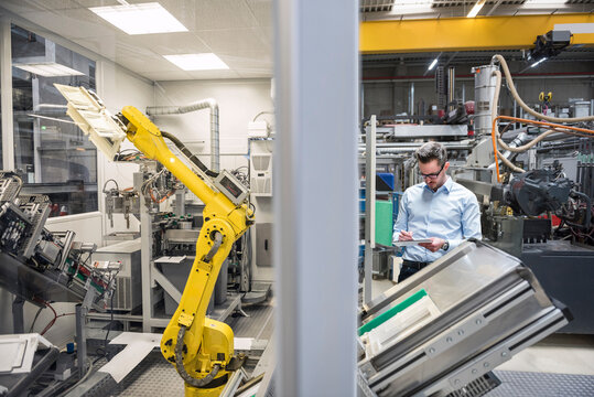Inspector examining robotics machine using tablet PC at factory