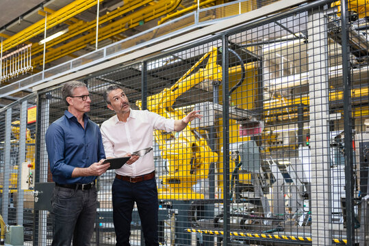 Businessmen operating machinery with tablet PC in factory
