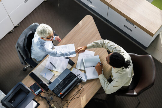 Interviewer shaking hands with candidate sitting at desk in office