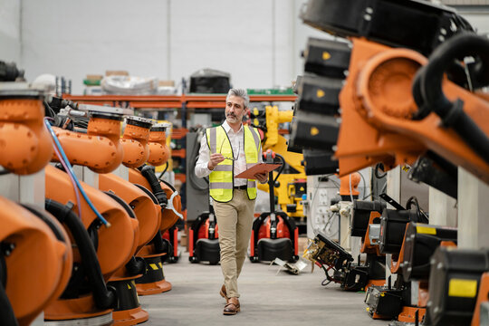 Engineer holding file folder and eyeglasses walking in factory