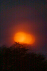 A warm orange orb emerges above the trees, illuminating the twilight sky with its ethereal glow