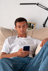 young man with mobile phone lying on sofa at home