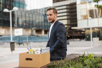 Businessman sitting with cardboard box outside office building