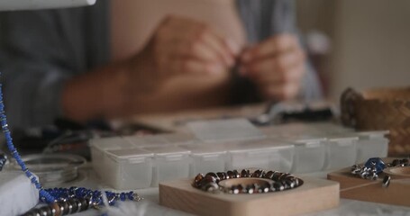 Close up of hands woman jewelry designer. She is sitting at a workspace with tools on it and is creating jewelry by stringing beads on fishing line. The process of creating jewelry. Small business. 