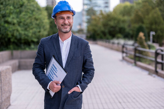 Smiling businessman wearing hardhat at footpath