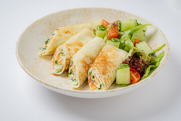 Rolled pancakes filled with assorted vegetables are served with a colorful green salad on the side