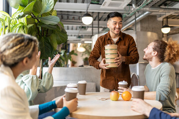 Smiling businessman holding stack of containers at lunch break in office