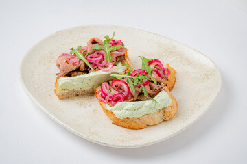 Roasted beef slices on toasted bread, adorned with creamy avocado spread and vibrant pickled onions