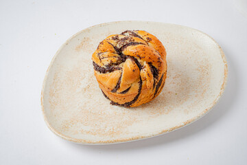 A sweet pastry with intricate swirls and poppy seeds rests elegantly on a rustic plate