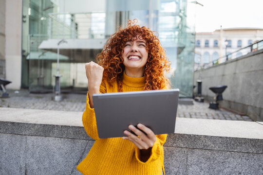 Excited redhead young woman with tablet PC gesturing fist