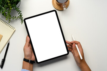Hands holding a tablet with a blank white screen and a stylus on a white desk