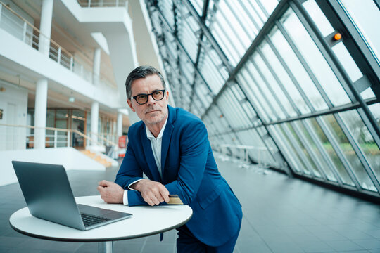 Thoughtful businessman with credit card leaning by laptop on table at office