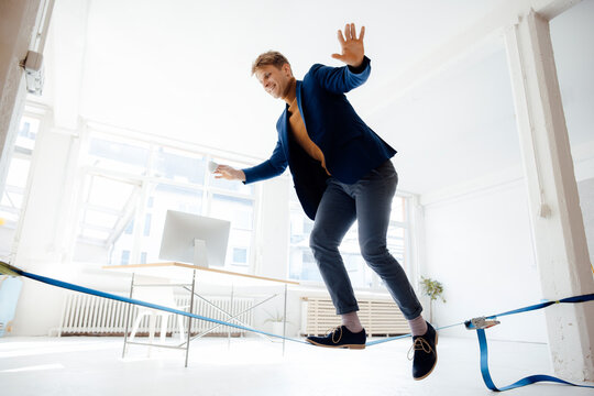 Happy businessman balancing on tightrope in office
