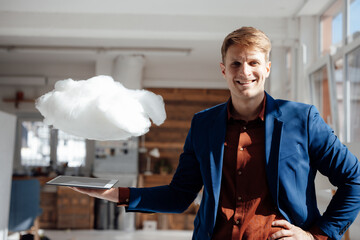 Happy businessman holding tablet PC under levitating cloud network in office