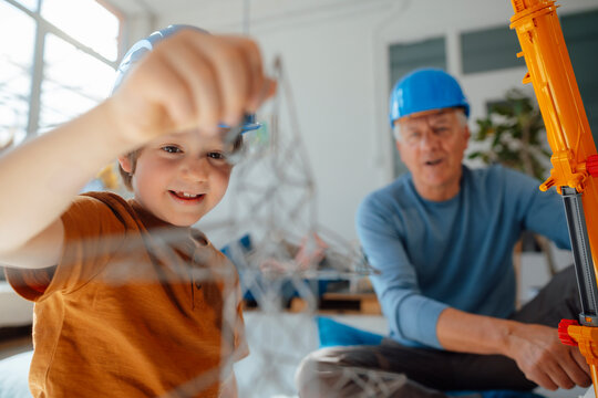 Boy examining electricity pylon model by grandfather at home