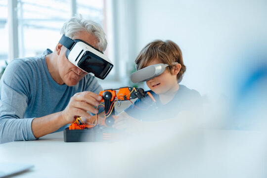 Senior man and grandson with futuristic glasses watching robot model at home