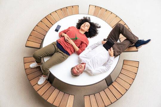Businessman by colleague holding wind turbine relaxing on table in office lobby