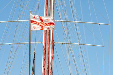 Flying High: Georgian Flag with Five Red Crosses on a Yacht Mast Against a Bright Blue Sky, Symbolizing National Pride and Maritime Adventures.