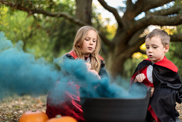 Kids in Halloween costumes sitting around a cauldron with blue smoke.