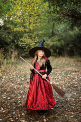Girl holding witch broom walking through forest. Halloween.
