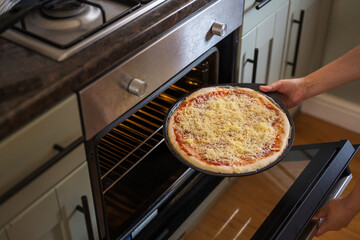 Female hand adding raw pizza to the oven, homemade pizza