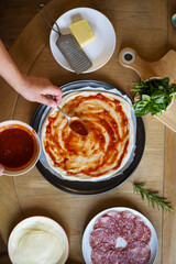 Cooking homemade pizza, adding tomato sauce to dough