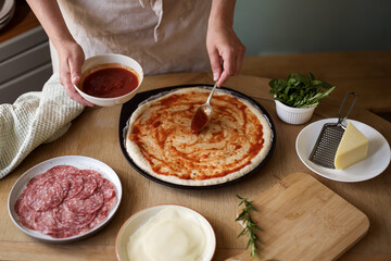 Cooking homemade pizza, adding tomato sauce to dough