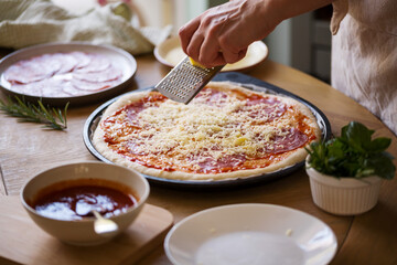 Woman's hands grate cheese over raw pizza, cooking at home