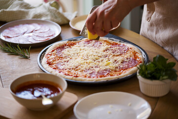 Woman's hands grate cheese over raw pizza, cooking at home