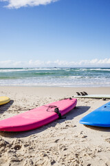 Colorful surfboards resting on sandy beach by ocean waves.