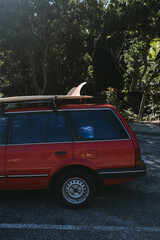 Red station wagon with surfboard parked near Byron Bay forest.