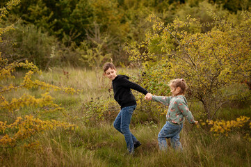Siblings running hand in hand through field.
