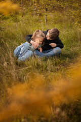 Siblings sitting on the autumn grass and tickling each other.