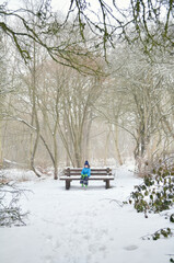 Toddler boy sitting on a bench in snowy park.