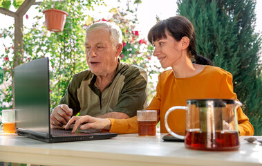 An elderly man and his daughter are sitting at a table with a laptop.
