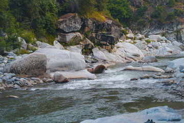The Swat River in KPK, featuring clear waters, large riverside boulders, and lush green foliage on the banks.