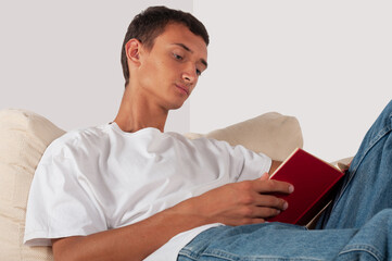 young man reading book on sofa at home