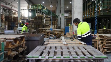 Skilled carpenter carefully disassembling wooden pallets using manual techniques within recycling facility environment, capturing industrial waste management process in slow motion