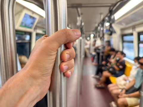 Bangkok, Thailand - June 22, 2025: Close up hand of Commuter holding handrail inside BTS skytrain during transit with seated passengers - Powered by Adobe