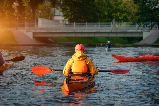 Participants paddle their kayaks on a calm river during training, wearing bright gear