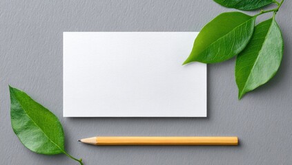 Blank notecard surrounded by green leaves and a pencil on a gray surface