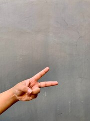 Close-up of a Woman hand showing peace sign on a gray concrete wall background.