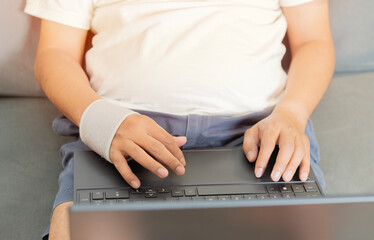 Cropped shot man with a wrist bandage is sitting on sofa and using laptop.