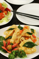 A close-up shot features crispy golden-fried fish  garnished with fresh curry leaves, red chilies, and a tomato-and-parsley garnish, served on a white plate