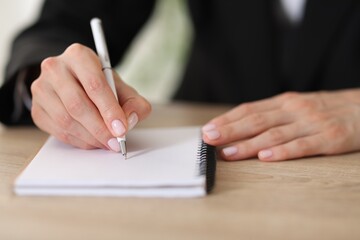 Woman writing in notepad with pen at wooden table, closeup