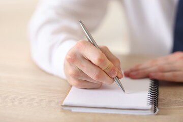 Man writing in notepad with pen at wooden table, closeup