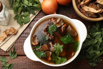 Tasty soup with mushrooms and parsley in bowl on wooden table, flat lay
