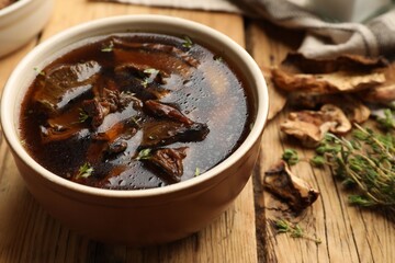Tasty soup with mushrooms and thyme in bowl on wooden table, closeup