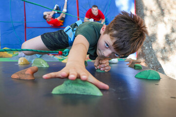 little preschool boy climbs on climbing wall route on holds with rope belay