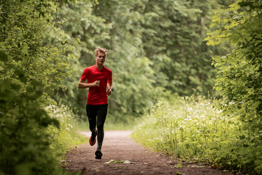 Young caucasian man running through green summer forest park.
